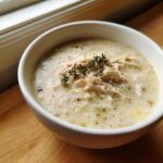 A close-up of a white bowl filled with creamy homemade cream of chicken soup, topped with shredded chicken and fresh thyme.