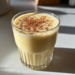 A glass of creamy, yellow homemade eggnog topped with a dusting of cinnamon spice.