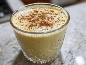 A close-up of a glass filled with creamy homemade eggnog, topped generously with ground cinnamon.