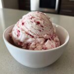 Two scoops of creamy, pink-swirled strawberry ice cream served in a white bowl.