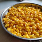 Close-up of bright yellow honey butter corn kernels glistening in a metal skillet.