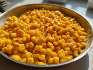 Close-up of sweet, glistening honey butter corn kernels cooked in a stainless steel skillet.