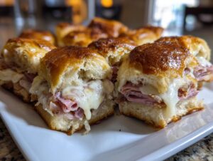 Close-up of several hot grinder sliders with melted white cheese dripping over ham on a white platter.