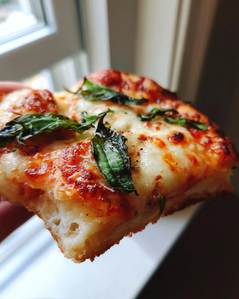 Close-up of a thick slice of pizza showing the fluffy keto pizza crust topped with melted cheese and fresh basil.