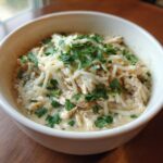 A close-up of a bowl of creamy keto white chicken chili topped with shredded white cheese and fresh chopped cilantro.