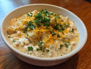 A close-up of a serving of creamy keto white chicken chili topped with shredded cheddar cheese and fresh parsley.