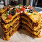 Cross-section view of a tall, layered Mexican pizza stacked with seasoned beef, melted cheese, and topped with fresh salsa, onions, and black olives.