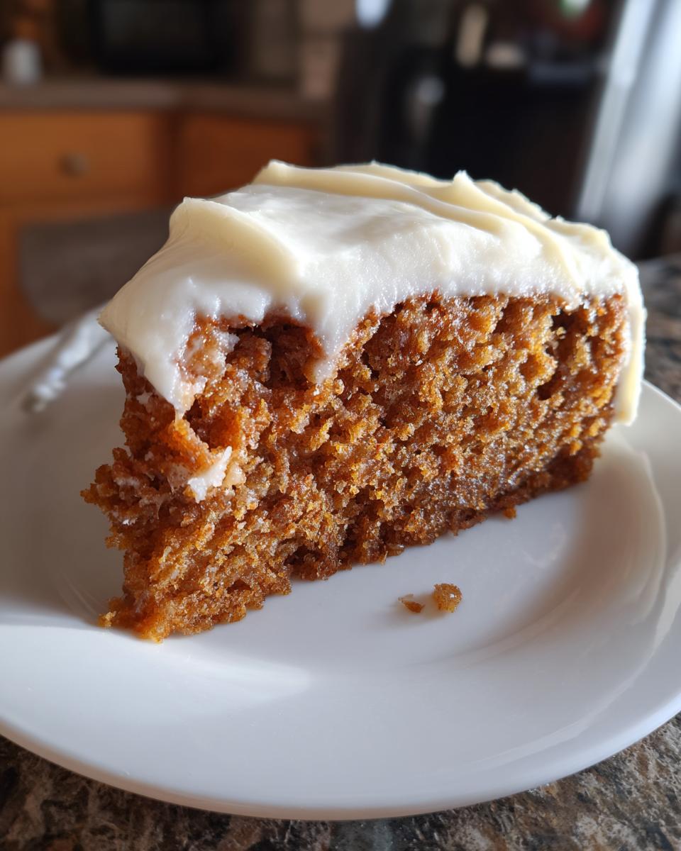 Close-up of a moist slice of applesauce cake topped with thick, white cream cheese frosting on a white plate.