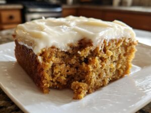 Close-up of a moist slice of applesauce cake topped with thick, creamy white frosting.