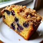 Close-up of a moist slice of blueberry bread featuring a golden crumb and a thick layer of brown sugar streusel topping.