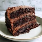 Close-up of a rich, moist slice of chocolate cake layered with thick chocolate frosting.