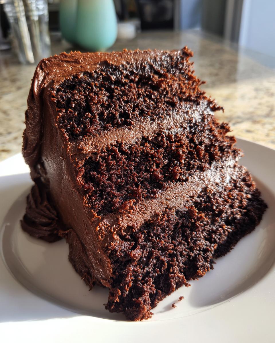 Close-up of a moist, dark slice of chocolate cake layered with rich chocolate frosting.