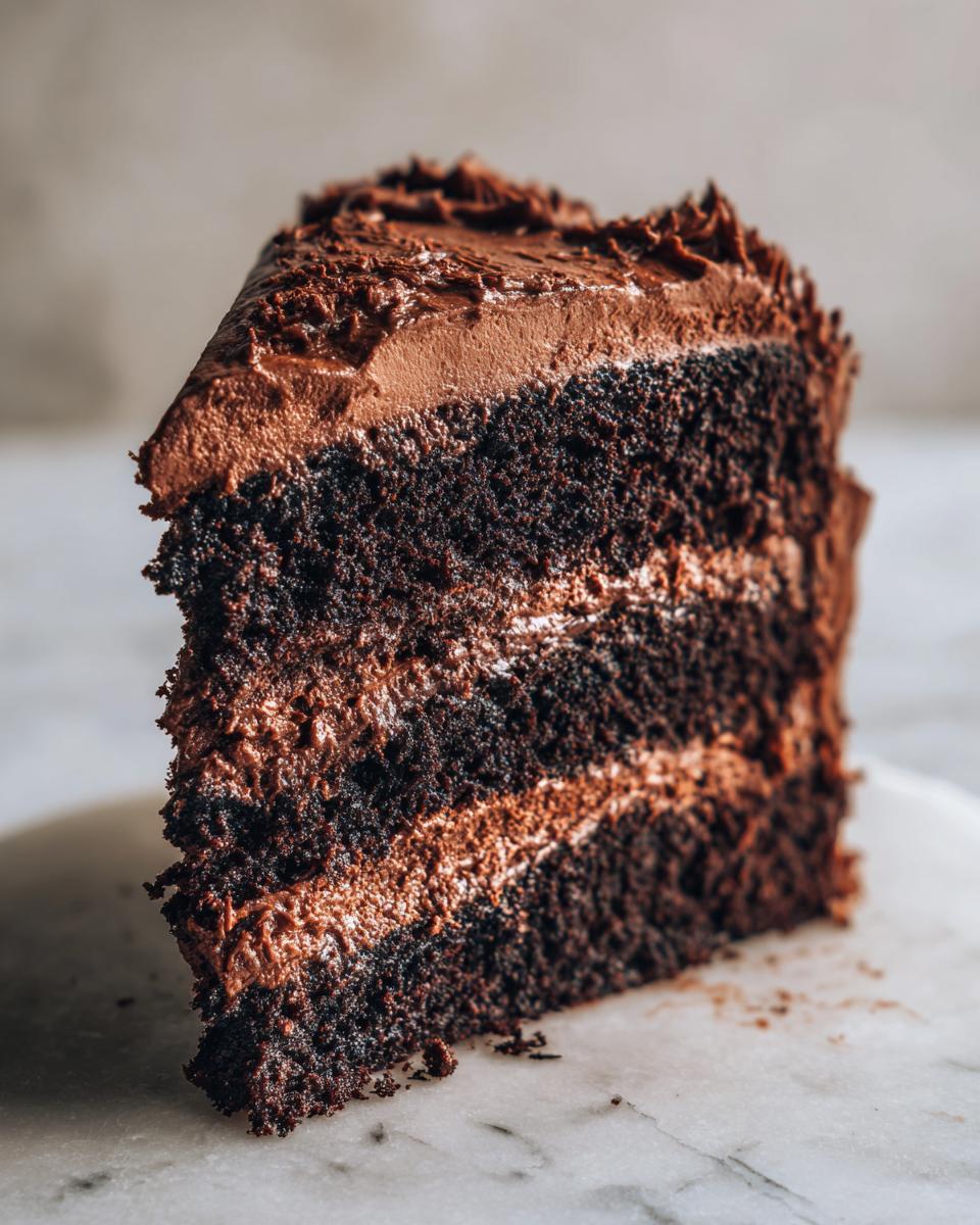 Close-up of a moist, dark chocolate cake slice with three layers of cake and two layers of chocolate frosting.