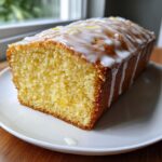 A close-up of a moist slice of lemon loaf cake topped with white glaze and lemon zest.