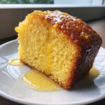 A close-up of a moist slice of orange juice cake, heavily drizzled with orange glaze and zest.