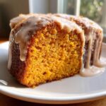 Close-up of a moist slice of sweet potato pound cake with a thick, creamy glaze dripping down the sides.