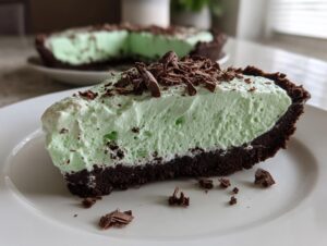 A close-up slice of no-bake grasshopper pie featuring a thick, light green filling and dark chocolate crust, topped with chocolate shavings.