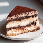 A perfect slice of no bake tiramisu cheesecake showing layers of cream, coffee-soaked cake, and a dusting of cocoa powder.
