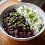 A close-up of a white bowl filled with rich, saucy black beans and rice, garnished with fresh cilantro.