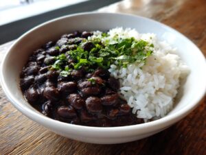 A close-up of a white bowl filled with rich, dark black beans and rice, garnished with fresh cilantro.