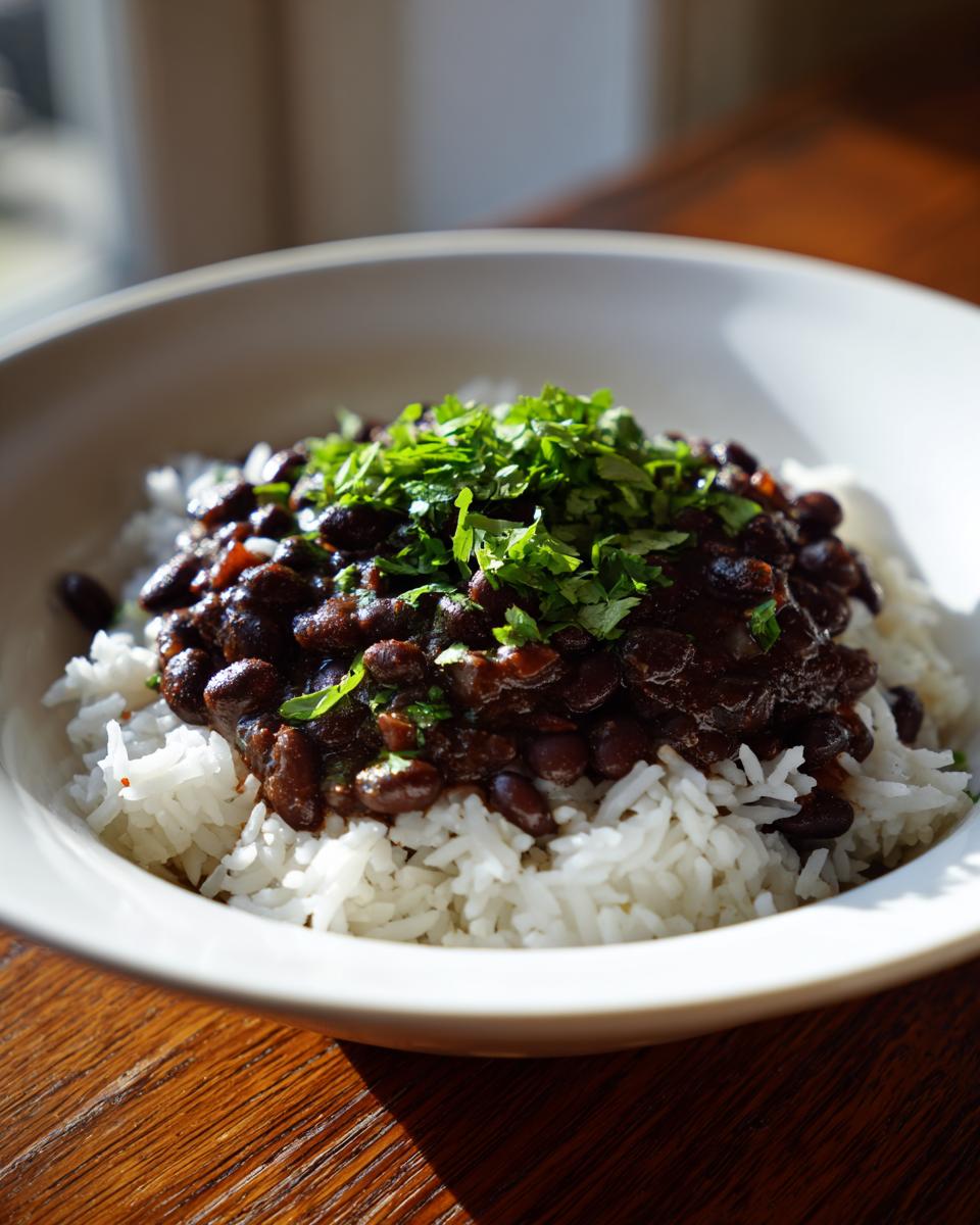 A close-up serving of fluffy white rice topped with rich black beans and rice mixture, garnished with fresh chopped cilantro.