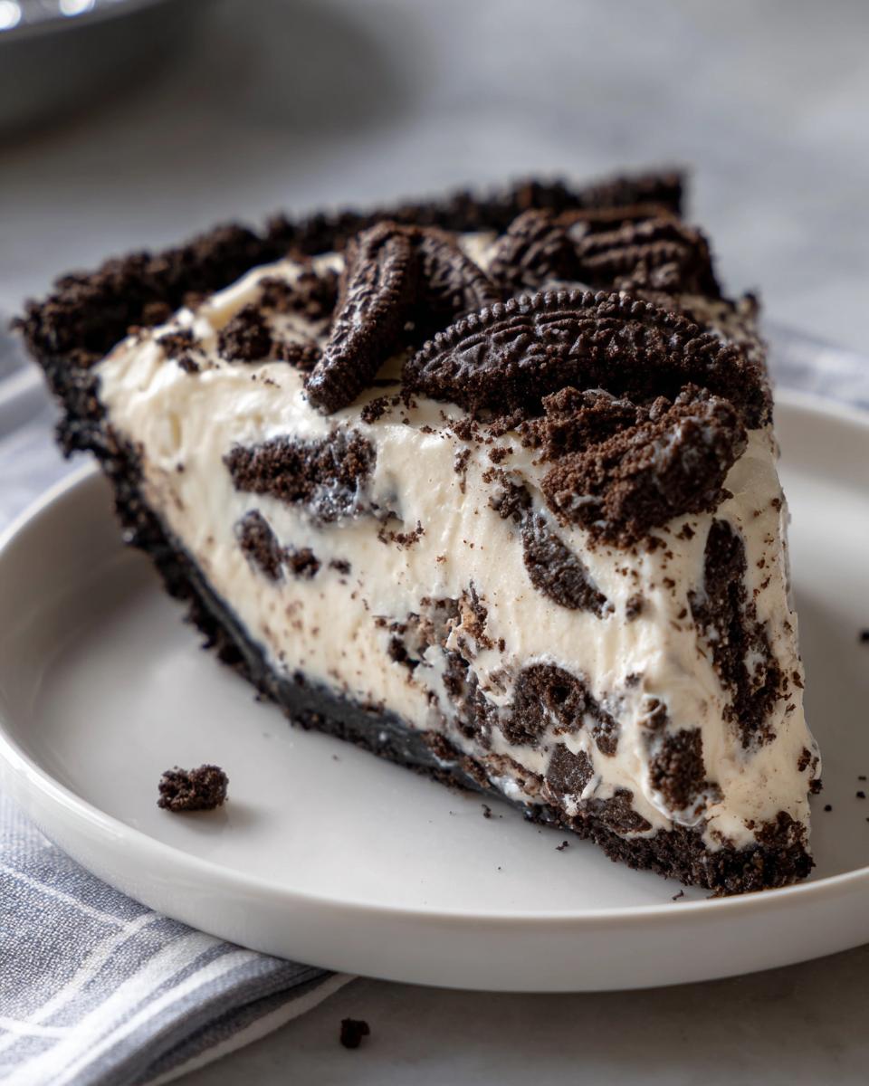 A generous slice of creamy Oreo pie featuring a dark chocolate crust and visible cookie chunks throughout the filling.
