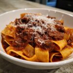 Close-up of wide pappardelle pasta generously topped with rich beef ragu and grated Parmesan cheese.