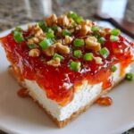A close-up slice of pepper jelly cheese dip showing a cream cheese base topped with bright red pepper jelly, walnuts, and chopped green onions.