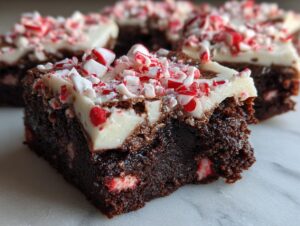 A close-up of a fudgy peppermint brownie square topped with white frosting and crushed candy canes.