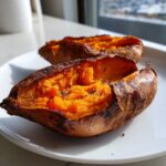 Close-up of a perfectly baked sweet potato split open, showing fluffy orange interior.
