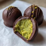 A close-up of delicious dubai chocolate balls, one cut in half revealing a bright green pistachio center.