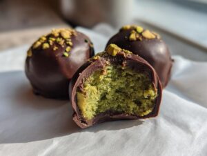 Close-up of dubai chocolate balls, one cut in half revealing a bright green pistachio center, topped with crushed nuts.