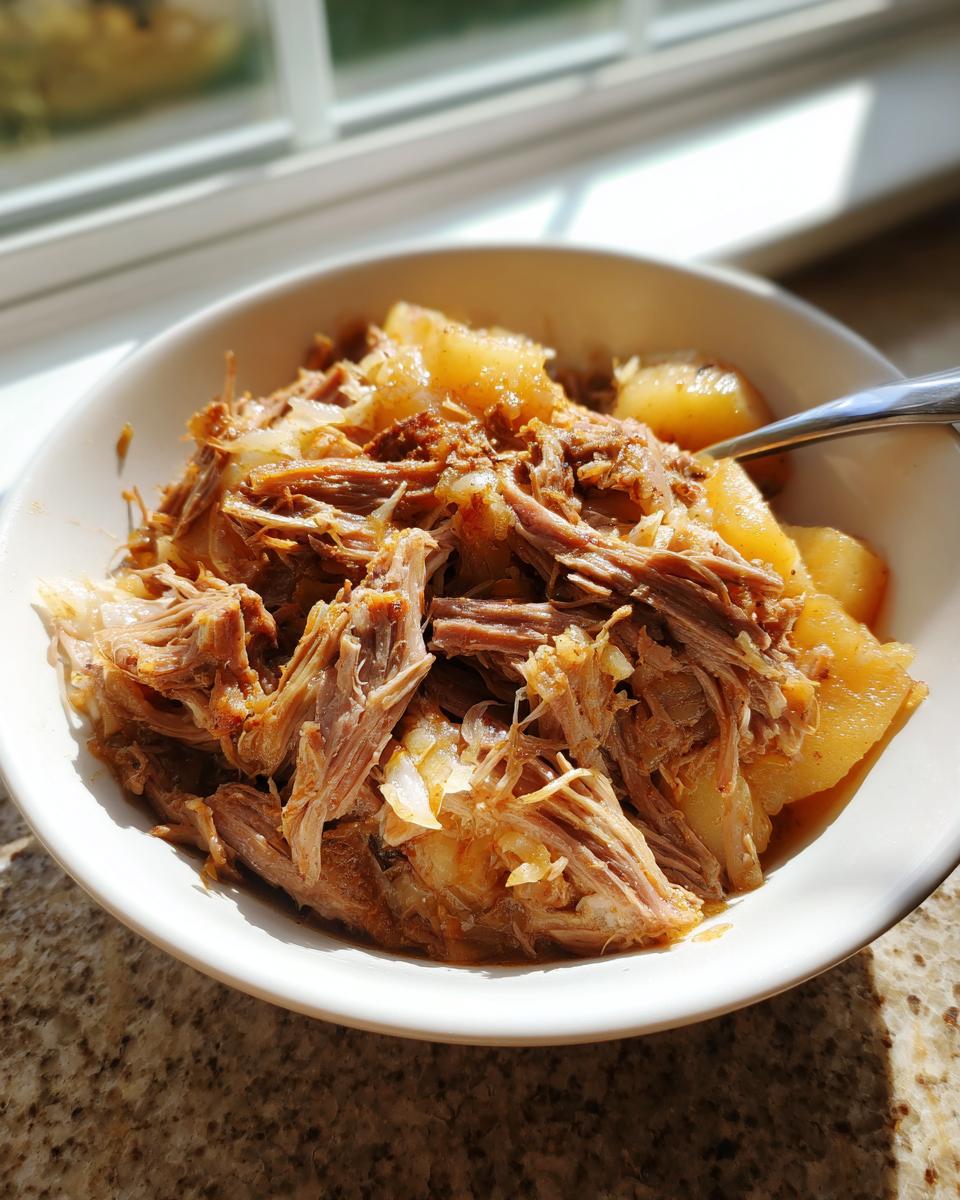 Close-up of a bowl filled with shredded pork and sauerkraut, served with chunks of potato or apple.