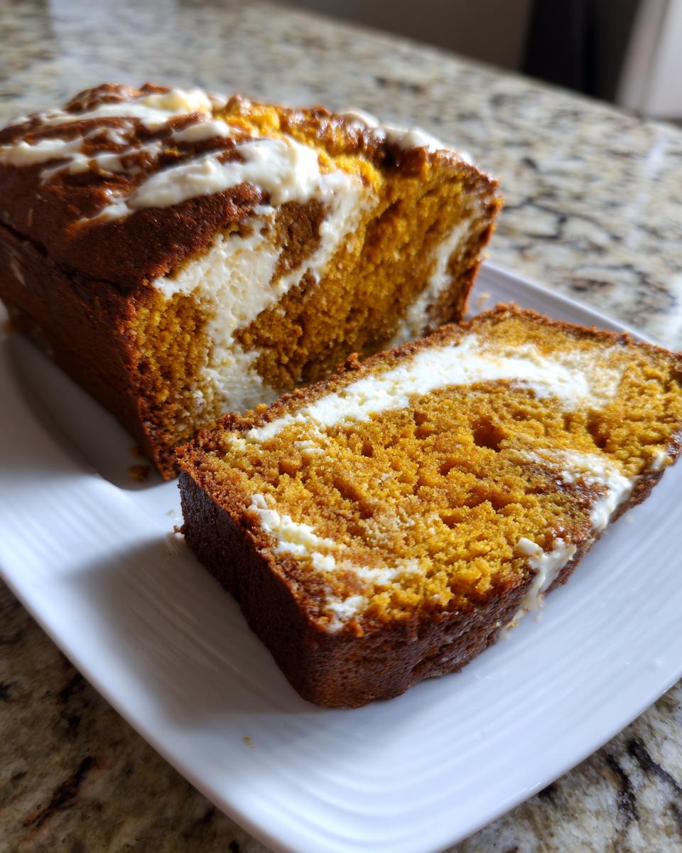A slice of moist pumpkin cream cheese bread showing the orange pumpkin swirl next to the white cream cheese filling.