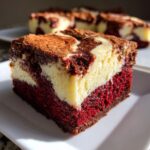 A single, thick square of red velvet cheesecake brownies showing distinct red cake, white cheesecake swirl, and dark brownie top.