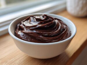 A close-up of thick, glossy chocolate fondue swirled high in a small white bowl.