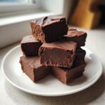 A stack of rich, dark chocolate fudge squares piled high on a white plate.