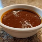 Close-up of rich, dark brown gravy in a small white bowl, perfect for serving with roasts.