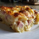 Close-up of a rich, creamy slice of scalloped potatoes and ham casserole with a golden-brown, cheesy crust.