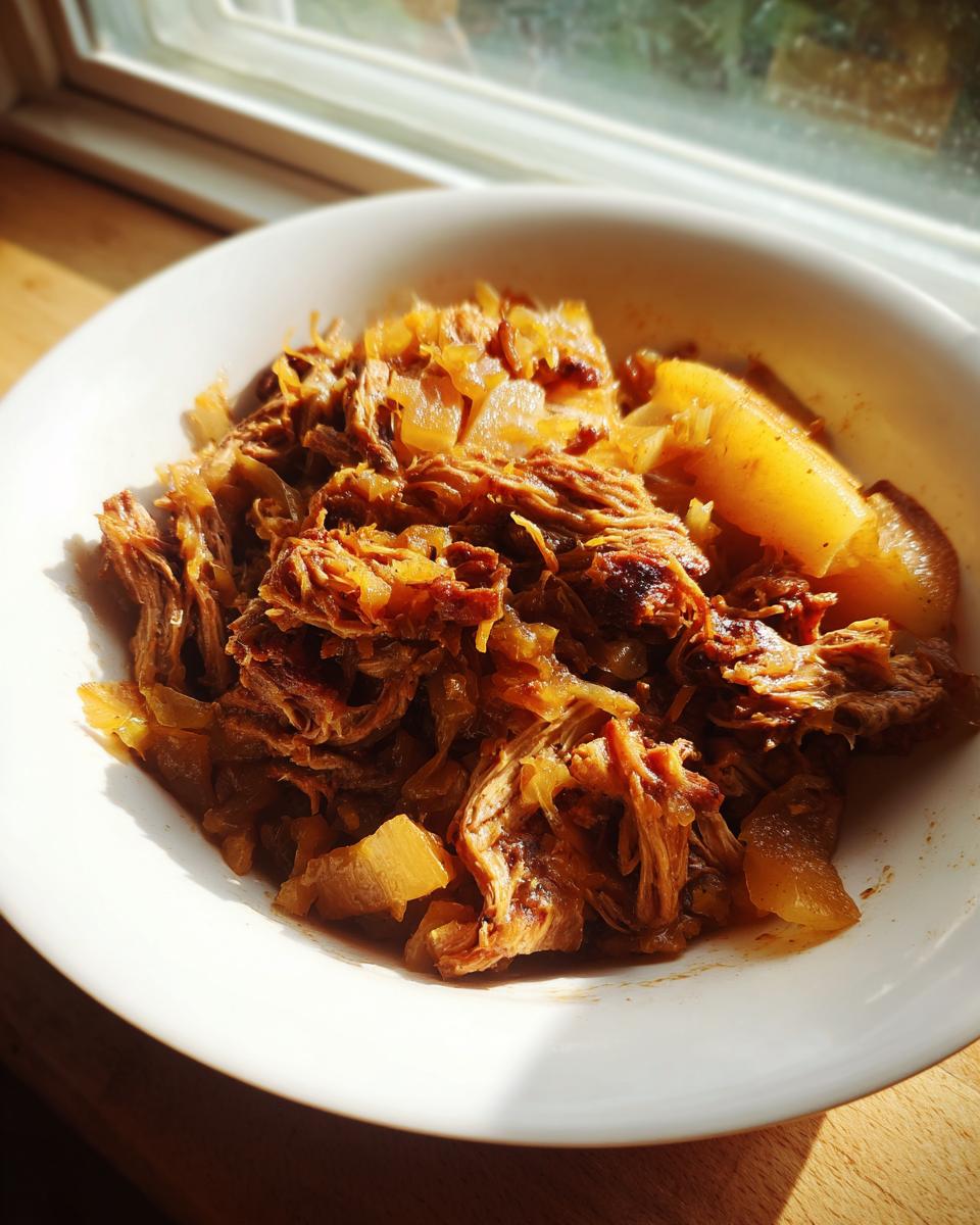 A close-up of shredded pork and sauerkraut mixture served in a white bowl, backlit by a window.
