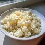 A white bowl filled with fluffy, seasoned cauliflower rice, brightly lit by natural sunlight.