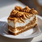 A perfect slice of layered biscoff cheesecake featuring a thick crust, white filling, and piped caramel-colored topping.