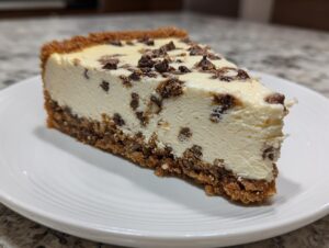 A perfect slice of creamy chocolate chip cheesecake with a thick graham cracker crust, served on a white plate.