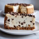 A thick slice of creamy chocolate chip cheesecake with a graham cracker crust, topped with mini chocolate chips.
