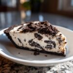 A close-up slice of creamy Oreo pie with chunks of chocolate cookie mixed in, sitting on a white plate.