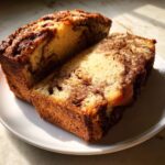 Two thick slices of moist cinnamon bread showing a beautiful swirl pattern, resting on a white plate.