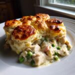 A serving of creamy slow cooker chicken pot pie topped with golden, fluffy biscuits on a white plate.