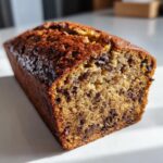 A close-up of a freshly baked loaf of sourdough banana bread studded with chocolate chips.