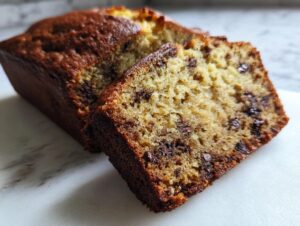 Close-up of a moist slice of sourdough banana bread with visible chocolate chips, next to the loaf.