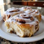 Close-up of four fluffy sourdough discard cinnamon rolls generously topped with white icing on a white plate.